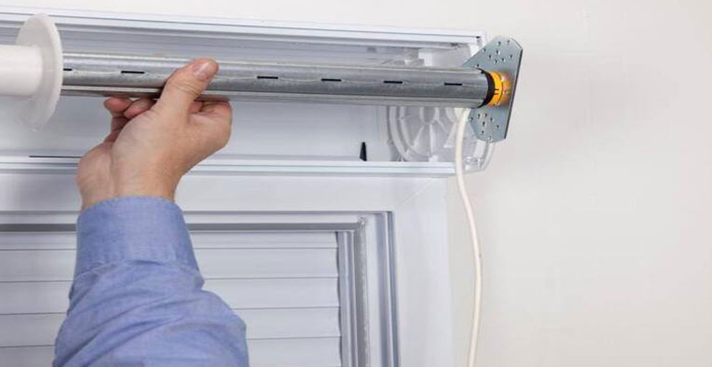 Artisan menuisier installant un moteur tubulaire dans le coffre ouvert d'un volet roulant, avec câblage électrique visible sur chantier de rénovation